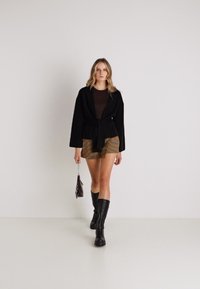 Čierna obopínajúca bunda cez hnedý top, spárovaná s károvanou mini sukňou. Model nosí čierne čižmy po kolená a drží malú metalickú tašku.