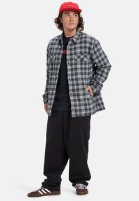 Czarno-szara koszula w kratę, z długimi rękawami, dwie kieszenie na piersi, noszona na czarnej koszulce. Zestawiona z luźnymi czarnymi spodniami i brązowymi trampkami.