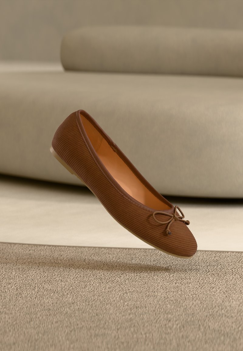 Chaussure plate marron en tissu côtelé, avec un bout arrondi et un nœud décoratif à l'avant. Intérieur lisse de couleur beige ; semelle plate et de couleur claire.