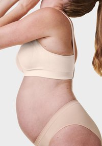 Beżowy zestaw biustonosza i majtek ciążowych z miękkiego materiału, bezszwowym wykończeniem i regulowanymi ramiączkami, podkreślający okrągły kształt brzuszka.