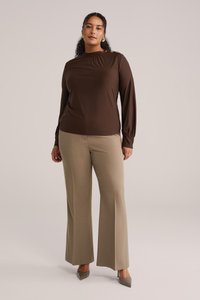 Maglietta marrone a maniche lunghe con scollo arricciato e bottoni laterali, abbinata a pantaloni beige a gamba larga, completata da décolleté grigie.