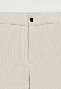 Tissu côtelé beige clair avec une fermeture à boutons sur le devant, présentant un détail fente sur le côté et une surface lisse et texturée.