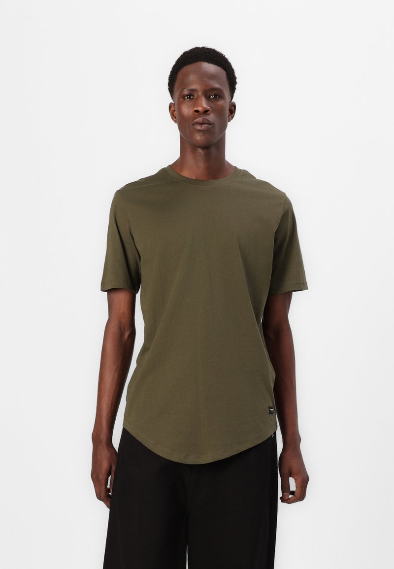 Tricou scurt cu mâneci scurte de culoare verde olives, fabricat din bumbac moale, având o guler în formă de cerc și un tiv rotunjit. Branding minim în colțul din stânga jos.