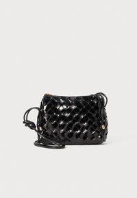 Černá lesklá prošívaná crossbody taška s uzlovými detaily na popruhu a zlatým zipem na jednolitém pozadí.