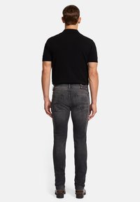 Schwarzes Poloshirt, getragen mit dunkelgrauen Slim-Fit-Jeans. Die Jeans verfügen über zwei Gesäßtaschen, Kontrastnähte und ein Lederetikett über dem Bund.