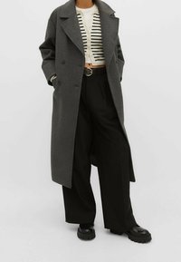 Gray wool blend trench coat, double-breasted design, relaxed fit, paired with a striped cardigan, high-waisted black trousers, and chunky black shoes.