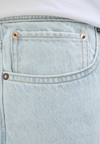 Vaaleansiniset farkkushortsit sisältävät takataskun, jossa on kupariset niitit ja hienovarainen vino tekstuuri, ommellut reunat ja siisti viimeistely.