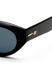 Óculos de sol pretos com lentes grandes e arredondadas. A armação tem um acabamento brilhante e apresenta um detalhe em dourado na parte externa da haste.