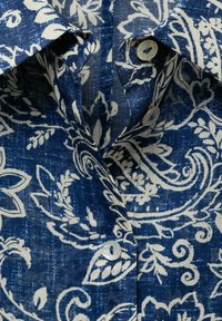 Camicia blu navy con bottone, con un motivo floreale bianco, caratterizzata da un tessuto testurizzato, colletto a punta e due bottoni sul davanti.