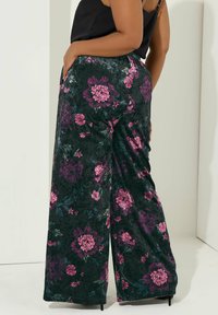 Blommiga vida byxor i mörkgrön sammet med rosa och lila blommönster, utrustade med sidofickor och en mjuk textur.