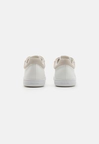Sneakers in pelle bianca con accenti in suede beige, suole basse e design minimalista. Presentano logo sul tallone e rivestimento interno in tessuto morbido.