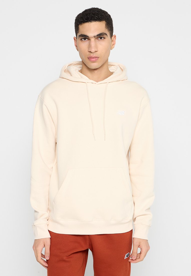 Hoodie beige clair en tissu doux, avec une poche frontale, un capuchon à cordon de serrage et un petit logo blanc sur la poitrine gauche.