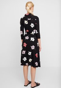 Black floral dress with three-quarter sleeves, featuring white, pink, and red flowers; includes a waist tie and a flowy skirt.