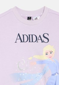 Λιλά φούτερ με το κείμενο "ADIDAS" και μια εικόνα της Έλσα από το Frozen της Disney να εκτοξεύει μαγεία πάγου με λαμπερές λεπτομέρειες.