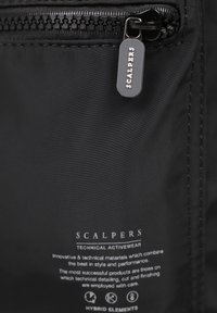 Bolsa de tela negra con cierre de cremallera, que presenta una etiqueta de logo, textura suave y detalles técnicos impresos en blanco en la parte inferior.