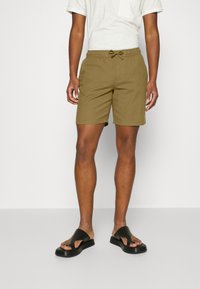 Shorts en coton kaki avec taille élastique et cordon de serrage. Associés à des sandales noires. Design simple sans motifs ni graphiques visibles.