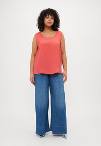 Coral sleeveless top with a rounded neckline, paired with wide-leg blue denim jeans featuring a flared hem and silver shoes.