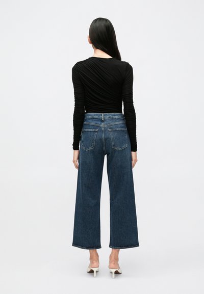 Temno modre široke jeans hlače z neobdelanim robom in klasičnim dizajnom s petimi žepi. Kombinirane s tesno prilegajočo črno dolgoročno majico.