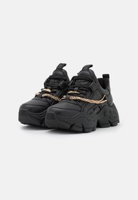 Black sneakers made of leather, featuring a chunky sole and a prominent gold chain detail across the laces. Rounded toe design.