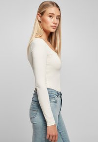 Top de manga larga, cuello redondo en blanco roto, hecho de una tela suave. Combinado con jeans ajustados de color azul claro, que muestran una silueta esbelta.