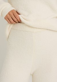 Ropa de descanso de tela blanca suave con un acabado texturizado. El conjunto incluye una camiseta de cuello redondo con puños sueltos, complementada con pantalones ajustados.