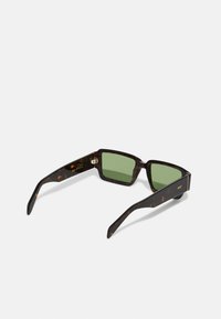 Occhiali da sole tartarugati con lenti verdi, forma rettangolare, montatura spessa e branding discreto sulla templi. Finitura opaca con design elegante.
