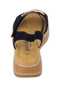 Sandali neri in suede con suola piatta color tan, caratterizzati da un design con una fascia incrociata e una soletta imbottita. Visibili dettagli in metallo color oro.