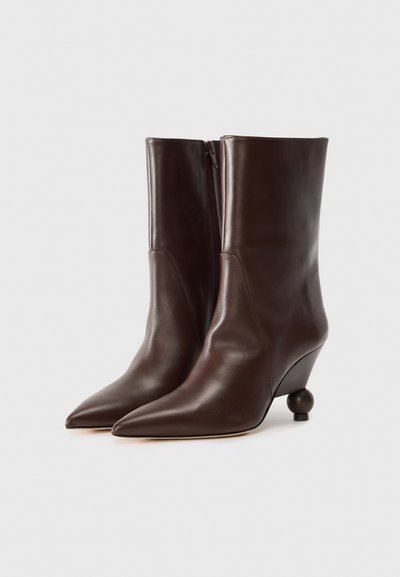 Brown leather ankle boots with a pointed toe, architectural wedge heel, and a side zipper detail. Smooth texture with a sleek design.