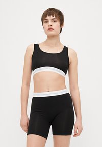 Svart topp och shortset i mjukt material, med ett vitt elastiskt band med varumärke runt midjan och bröstet. Enkel design.