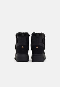 Schwarze isolierte Stiefel mit Kunstfellbesatz, robuster Gummisohle und auffälligen Logoprunen auf der Rückseite. Strukturierter Stoff mit glatter Oberfläche.