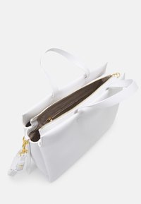 Sac à main en cuir blanc avec deux poignées, fermeture éclair dorée sur un compartiment central, et une bandoulière amovible avec des éléments dorés.