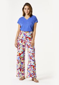 Blaues V-Ausschnitt-T-Shirt kombiniert mit einer weiten Hose, die ein farbenfrohes Blumenmuster in Rot, Pink, Blau und Beige zeigt. Sandalen runden den Look ab.