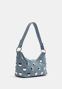 Modra semišna torbica z debelim trakom in velikimi okroglimi srebrnimi zakovicami, ki enakomerno prekrivajo njeno površino.