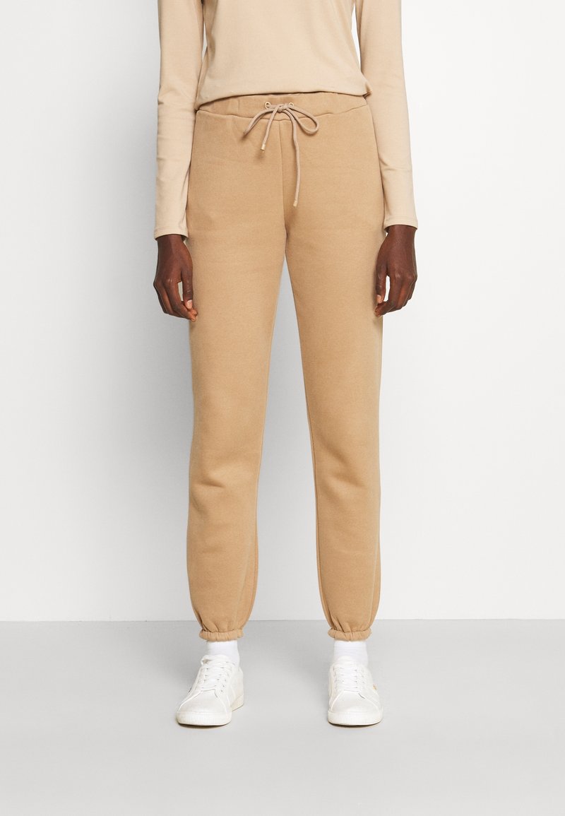 Beżowe dresy wykonane z miękkiego materiału, z elastycznym paskiem w talii ze sznurkiem, dopasowanymi ściągaczami i gładką fakturą.