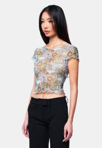 Genomskinlig, kort topp med en pastelldesign som återspeglar djur, blommor och dödskallar. Volangkanter och en mjuk textur. Bärs med svarta byxor.