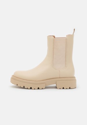 Bottines beiges avec un dessus en cuir texturé, des panneaux élastiques sur les côtés et une semelle en caoutchouc épaisse avec un motif de crampons.