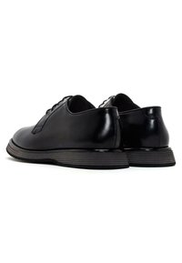 Chaussures en cuir noir avec une surface lisse, de forme arrondie, à lacets et semelles en caoutchouc noir nervuré. Style simple et moderne.