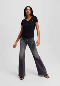 Tricou negru cu mânecă scurtă și decolteu în V, având un logo albastru, asortat cu blugi gri din denim cu talie înaltă, evazați, care au nasturi în față și o finisare estompată.