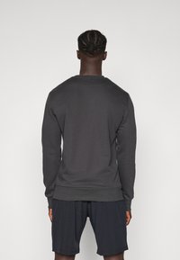 Felpa grigia scura con scollatura rotonda, polsini e orlo a coste. Vestibilità casual, mostrata da dietro, abbinata a pantaloni corti scuri.