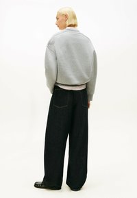 Felpa grigia oversize con polsini a coste, abbinata a jeans scuri a gamba larga con tasche posteriori e dettagli di cucitura minimi.