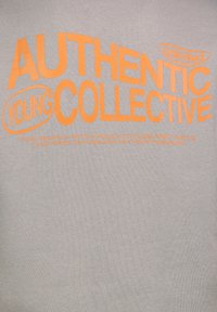 Grauer Sweatshirt mit großen orangenen Texten "AUTHENTIC YOUNG COLLECTIVE" und zusätzlichem kleinerem Text darunter. Weiche Textur.