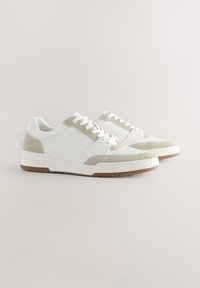 Hvide lædersneakers med beige ruskindsdetaljer, rund tå, flad sål og matchende snørebånd. Enkelt design med teksturerede materialer og syningsdetaljer.