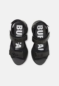 Sandales noires avec des brides réglables et une semelle texturée. Présente le texte "BUFFALO" en blanc sur le pied et les straps.