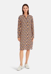 Bedrucktes Hemdkleid in bunten geometrischen Mustern; mit Kragen, langen Ärmeln, aus leichtem Stoff, kombiniert mit weißen Slippern.