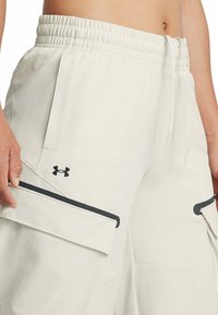 Gai bēškrāsas kravas bikses ar elastīgu jostu, šnēriņu un melnām akcentiem. Iekļautas divas lielas sānu kabatas un "Under Armour" logo.
