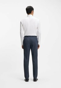 Witte overhemd met knopen en donkergrijze, op maat gemaakte broek, met een gladde stof, rechte pasvorm en subtiele textuur. Zwarte schoenen maken de outfit compleet.