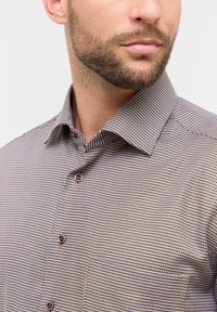 Camicia con motivo marrone e bianco, con colletto strutturato, caratterizzata da bottoni marroni e un tessuto texturizzato.