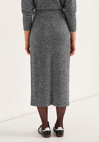 Grijze gebreide jurk met een ribbelstructuur, lange mouwen en een slits achteraan. Gepaard met zwart-witte sneakers met gestreepte accenten.