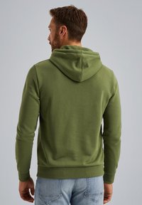 Felpa verde con cappuccio realizzata in tessuto morbido, dotata di tasca a marsupio e polsini a costine, abbinata a jeans blu.