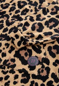 Leopard print fabric in tan, black, and brown. Soft texture with a rounded label featuring "NEXT" and active wear details. Folded design.